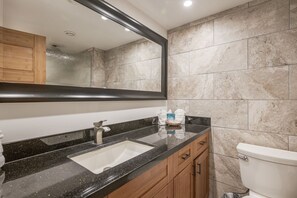 Une salle de bain avec un comptoir en granit noir, un lavabo blanc, un miroir et des toilettes.