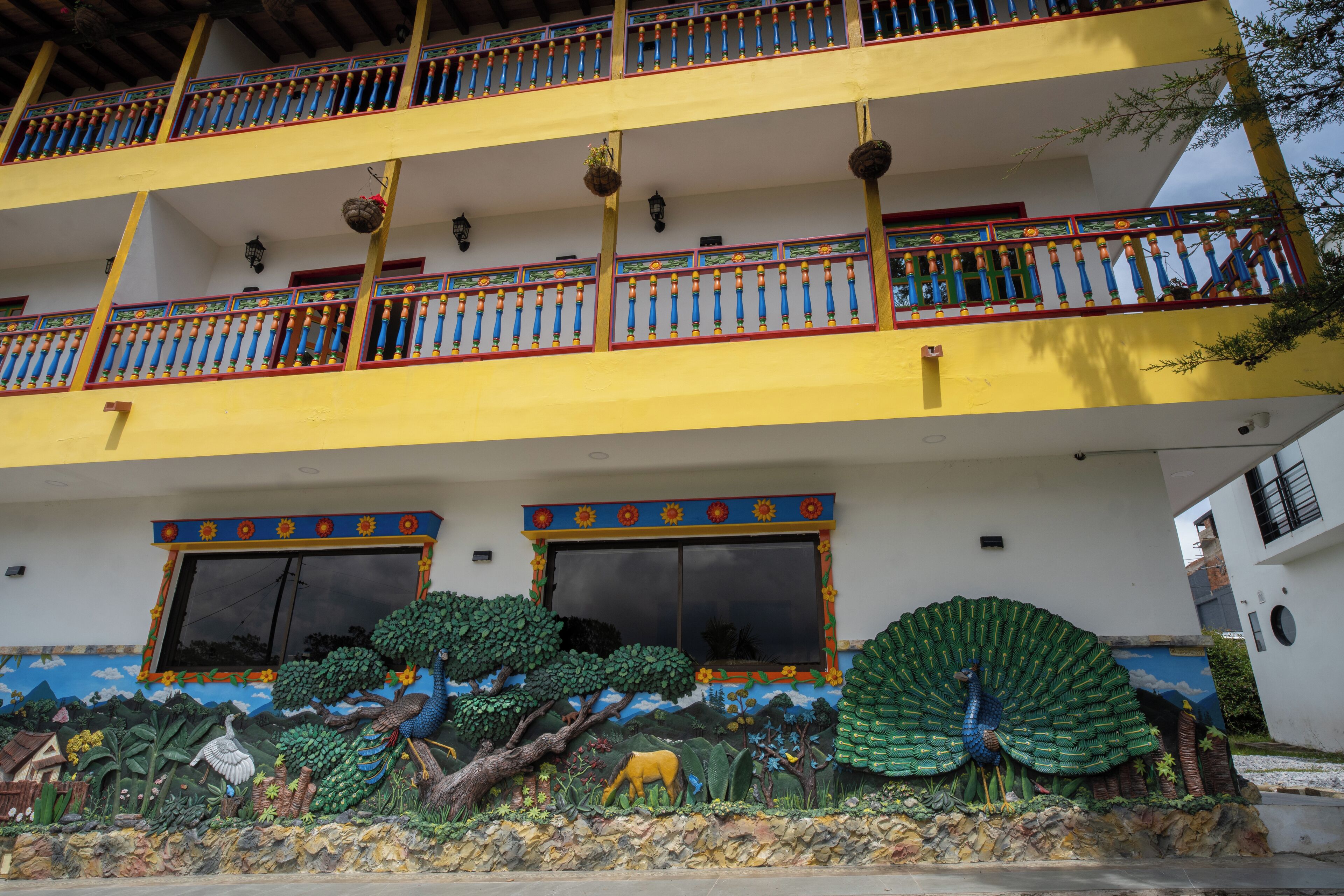 Un immeuble à plusieurs étages doté de balcons, de grandes fenêtres et d’une fresque représentant un paysage tropical.