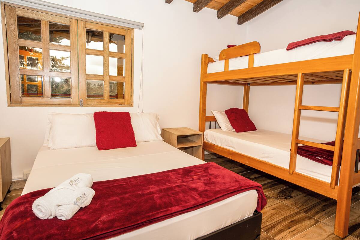 Una stanza con un letto, una finestra e una cuccetta in legno, con una coperta rossa.