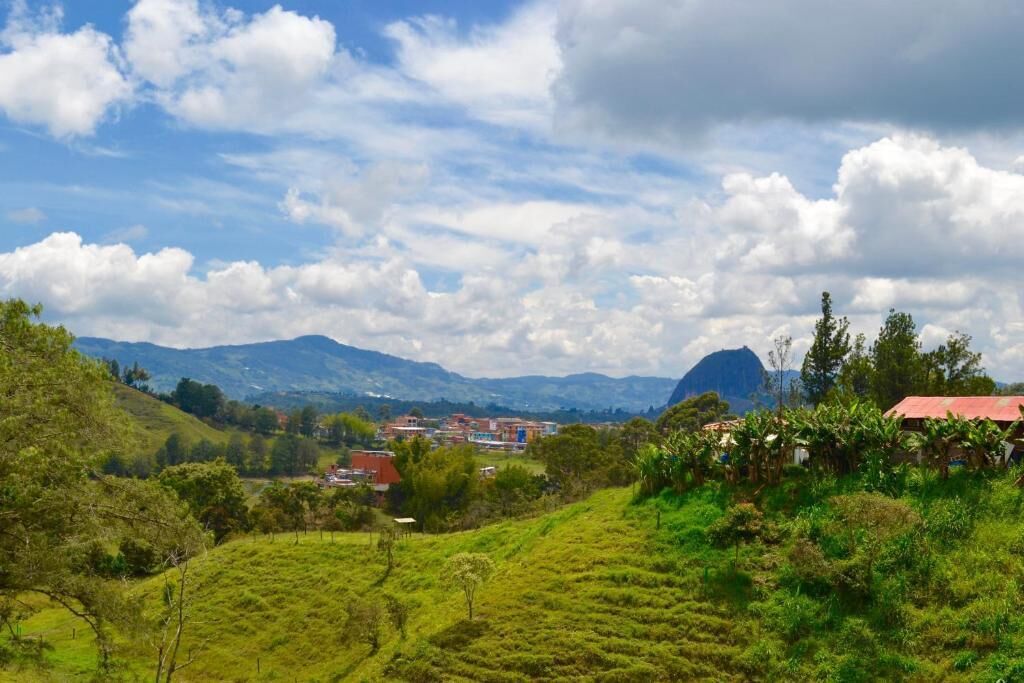Un paysage verdoyant et luxuriant, avec des collines ondoyantes, une montagne en arrière-plan et un petit village aux bâtiments aux toits rouges.