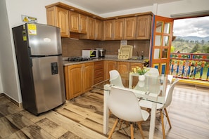 A kitchen with wooden cabinets, a stainless steel refrigerator, a microwave, and a dining area with a glass table and chairs. - ROBLE COLONIAL  (Guatape)