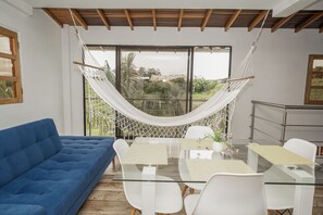 A modern room with a glass table, white chairs, a blue sofa, and a hammock. - ROBLE COLONIAL  (Guatape)