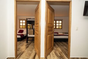 A room with two beds, a bunk bed, wooden flooring, and a TV mounted on the wall. - ROBLE COLONIAL  (Guatape)