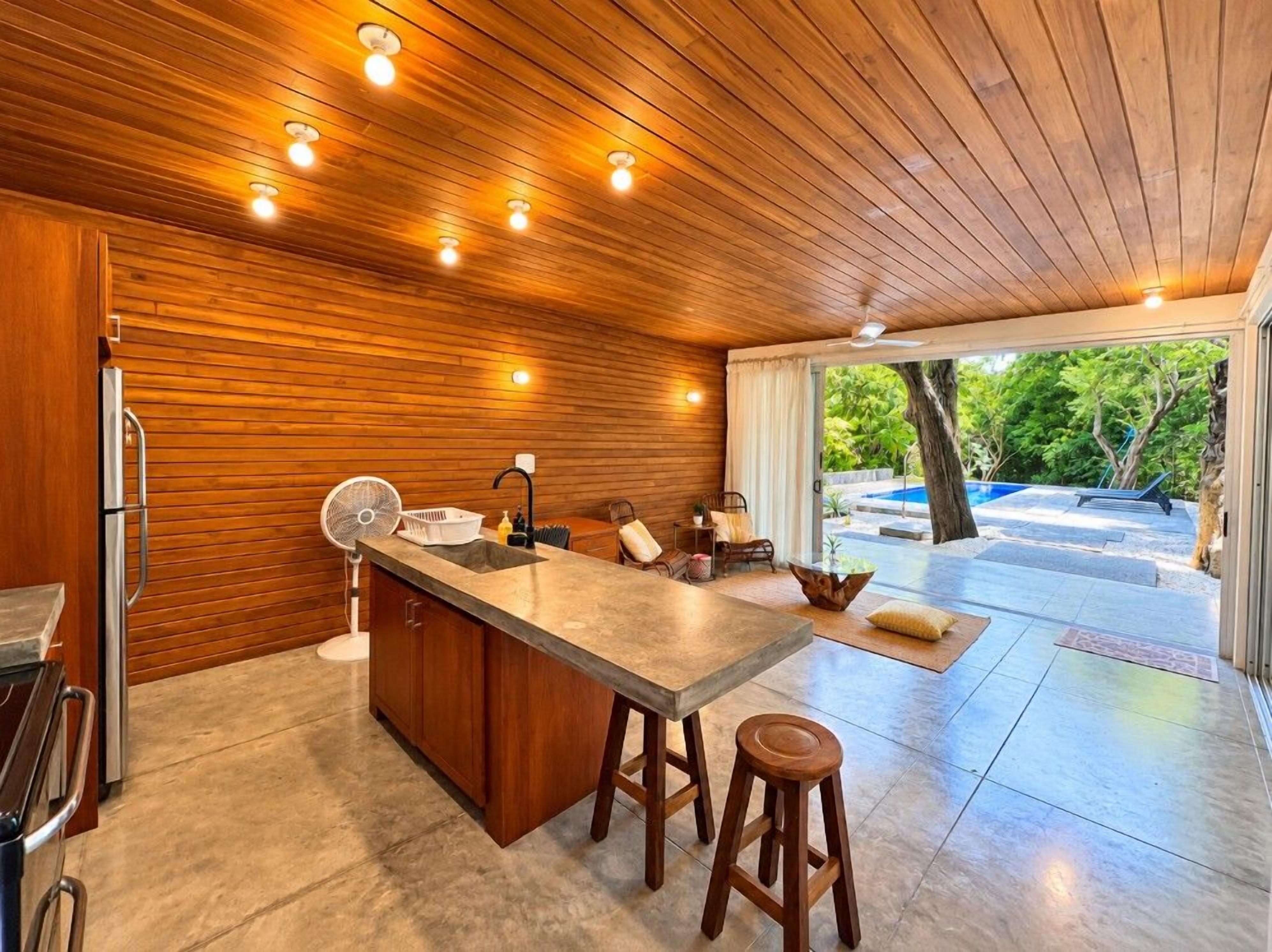 Une cuisine moderne avec des murs en bois, un îlot central doté de tabourets et une vue sur l’extérieur.