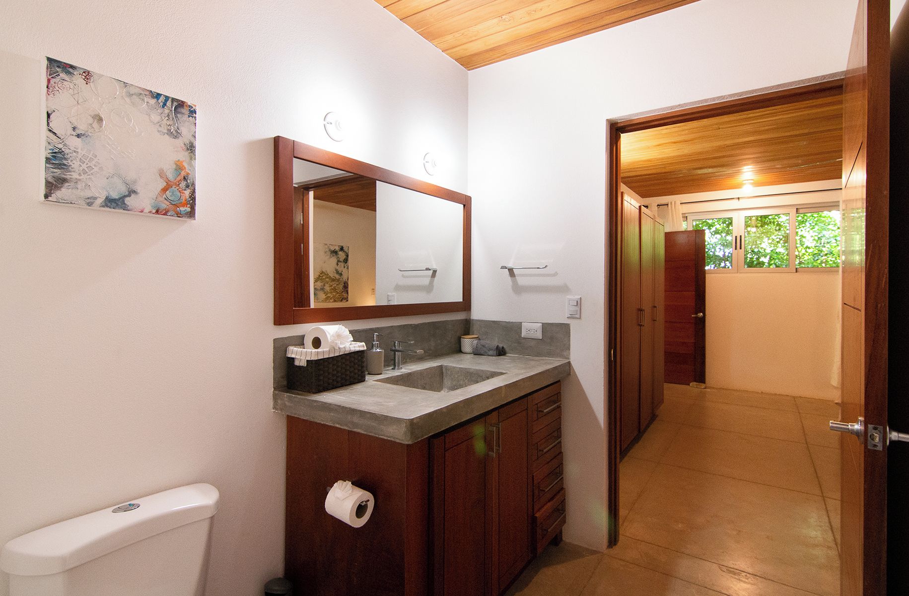 Een badkamer met een houten wastafelmeubel, een grote spiegel, een toilet en een wastafel.