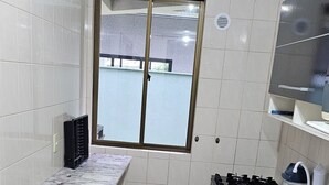 Cuina petita amb parets revestides de rajoles blanques, una finestra, un fogó integrat i un frigorífic.