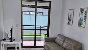 Un saló amb un sofà beix, una taula blanca i un gran finestral corredís que dona a un balcó.