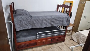 Un llit superposat amb estructura de fusta, roba de llit gris i un petit tabernacle de fusta.