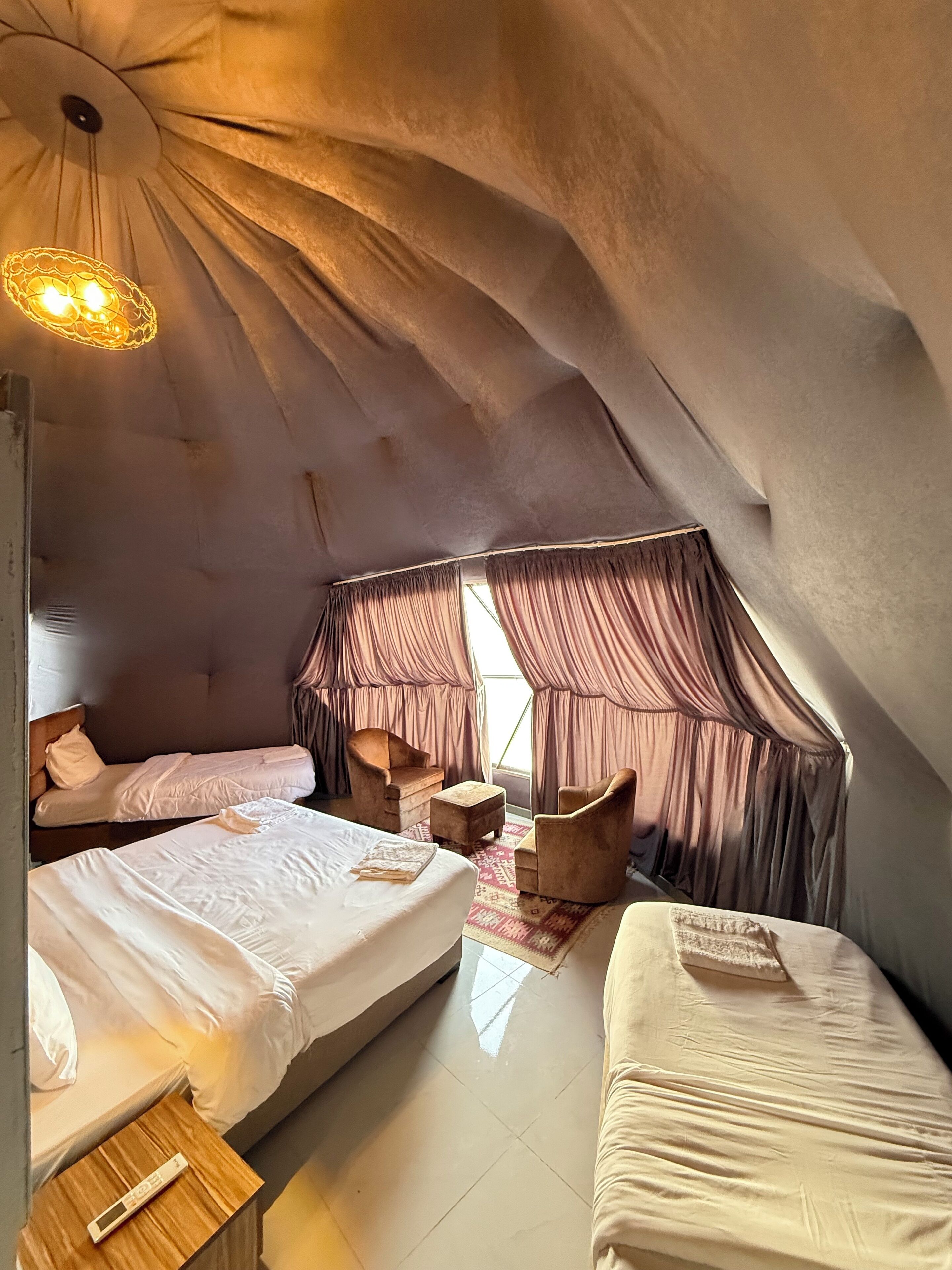 A cozy, triangular room with two beds, a small table, and a chair.