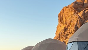 A row of dome-shaped tents with large windows, set against a desert backdrop with rocky formations. - Arjowana Luxury Camp (Wadi Rum)