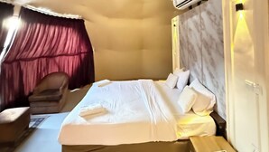 A bedroom with a large bed, a bedside table, a chair, an air conditioning unit, and a ceiling light fixture. - Arjowana Luxury Camp (Wadi Rum)