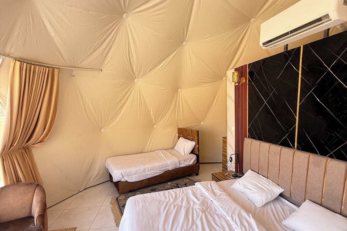 Habitación tipo tienda de campaña con dos camas, una silla y un equipo de aire acondicionado.