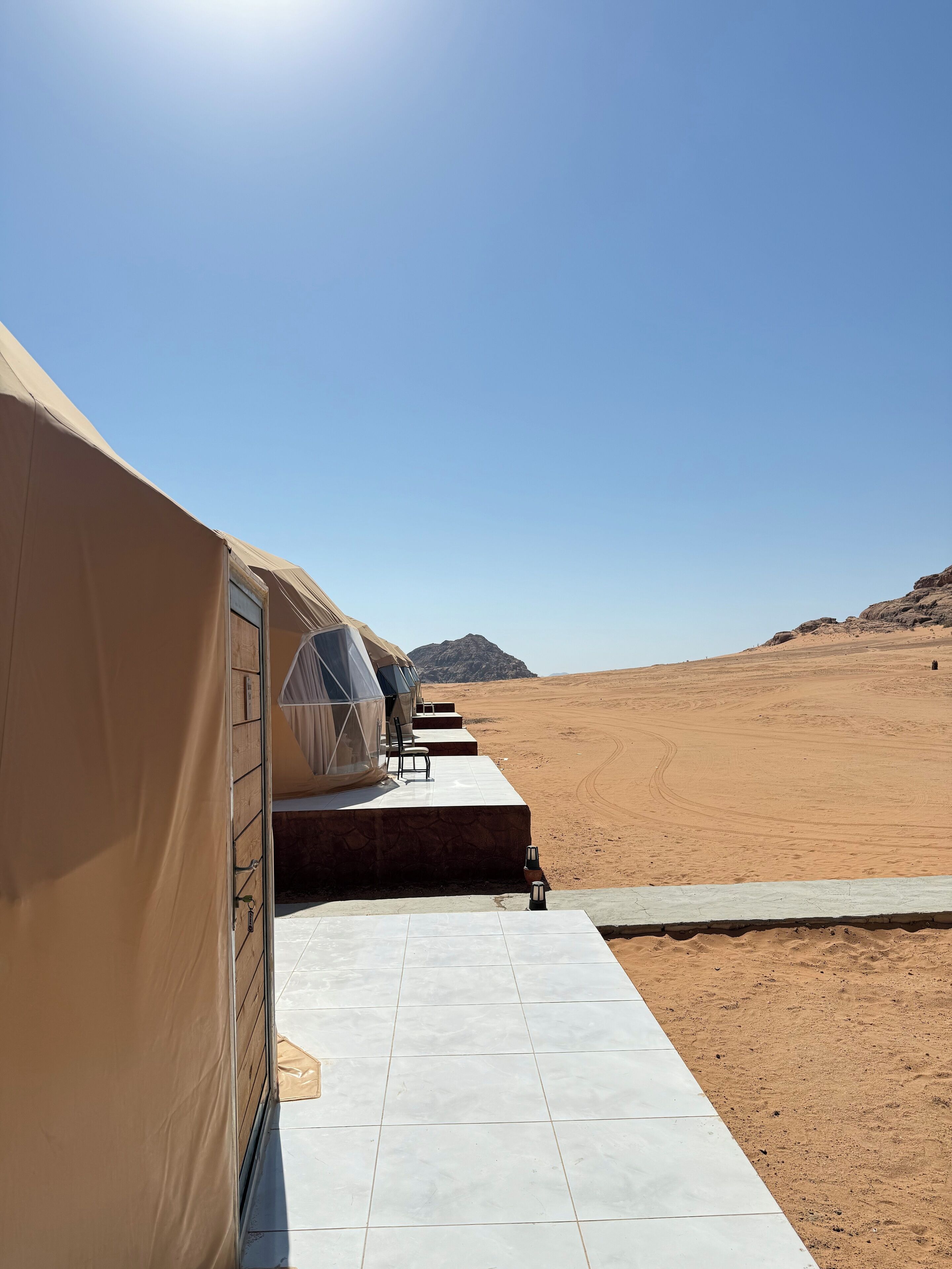 A desert landscape with a row of beige tents, each with a small table and chairs.