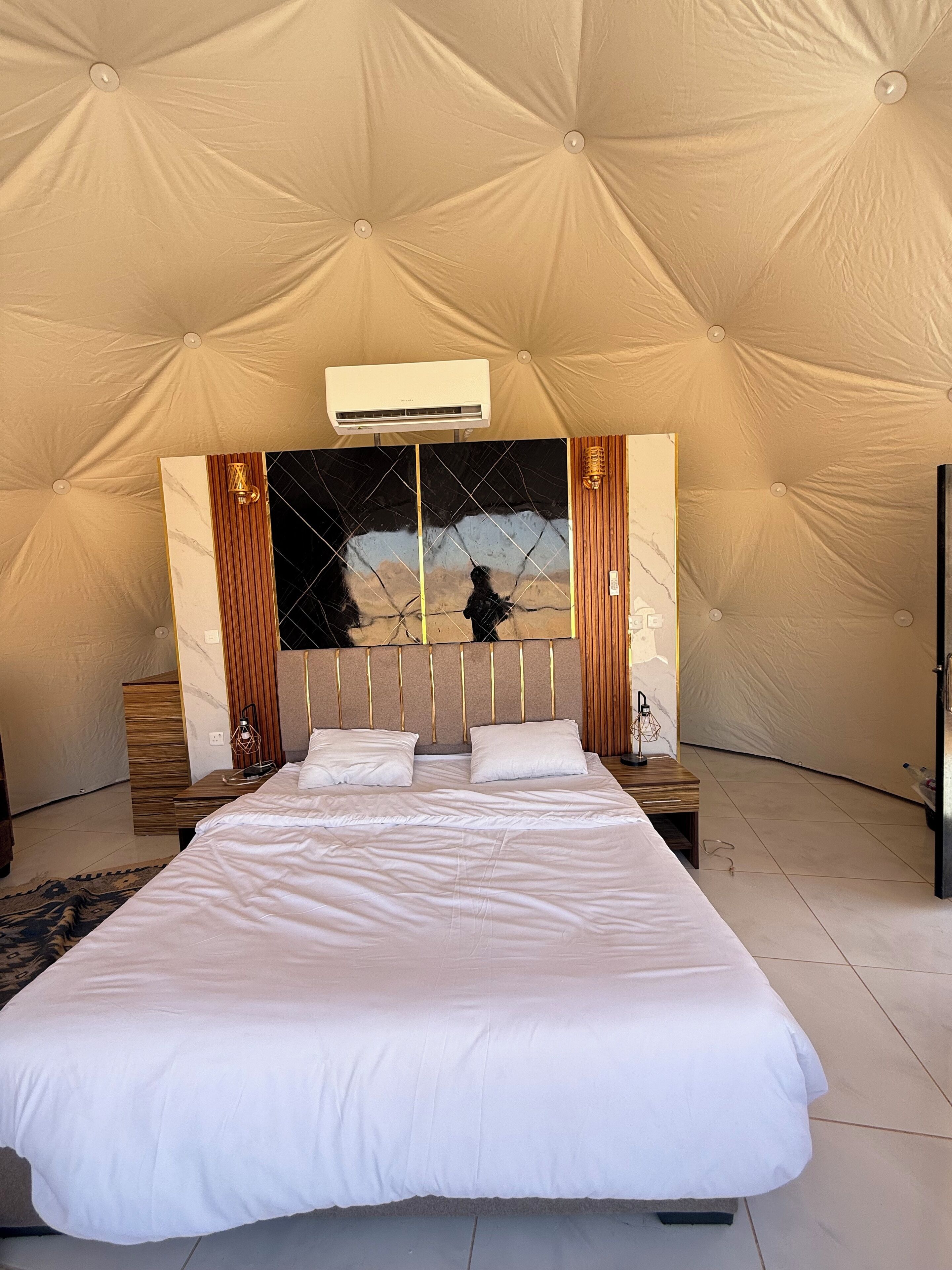 A spacious tented room with a large bed, a wall-mounted air conditioner, and a decorative mirror.