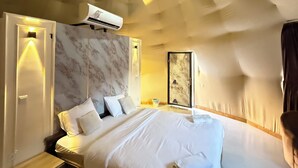 A modern bedroom with a marble headboard, a large bed, bedside tables, and a ceiling light fixture. - Arjowana Luxury Camp (Wadi Rum)