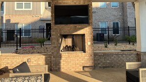 A covered patio with a brick fireplace, outdoor seating, and a ceiling fan.