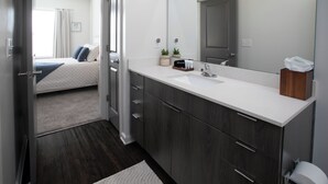 A modern bathroom with a white countertop, dark wood cabinets, and a large mirror.