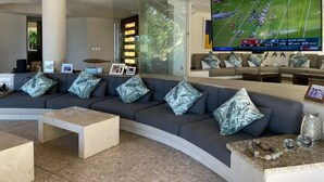 Een moderne woonkamer met een gebogen grijze bank, een flatscreen televisie en een glazen scheidingswand.