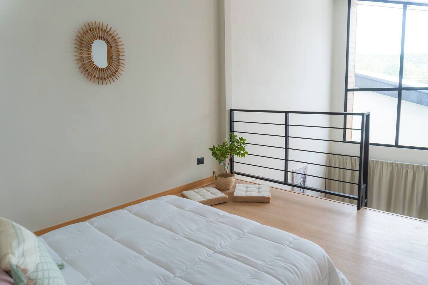 A bedroom with a bed, a window with a view, a plant, and a decorative mirror.
