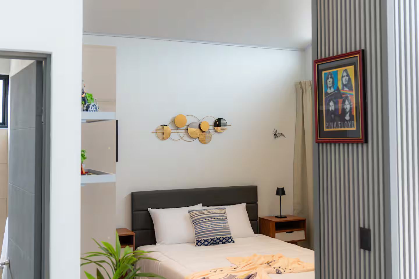 Une chambre à coucher comprenant un lit, des tables de chevet, une lampe fixée au mur, un tableau encadré et un élément décoratif mural.