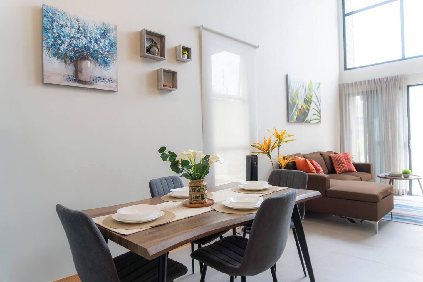 Una sala de estar moderna con zona de comedor. Hay dos sofás, una mesa de centro y una mesa de comedor servida con platos y un jarrón de flores.