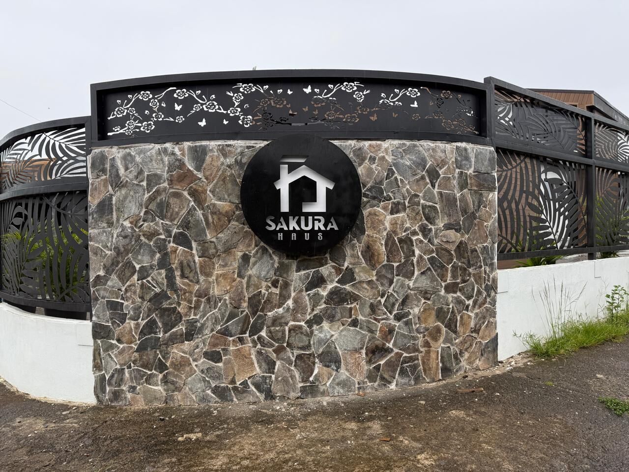 A stone wall with a circular logo for "Sakura Haus" and decorative metalwork.