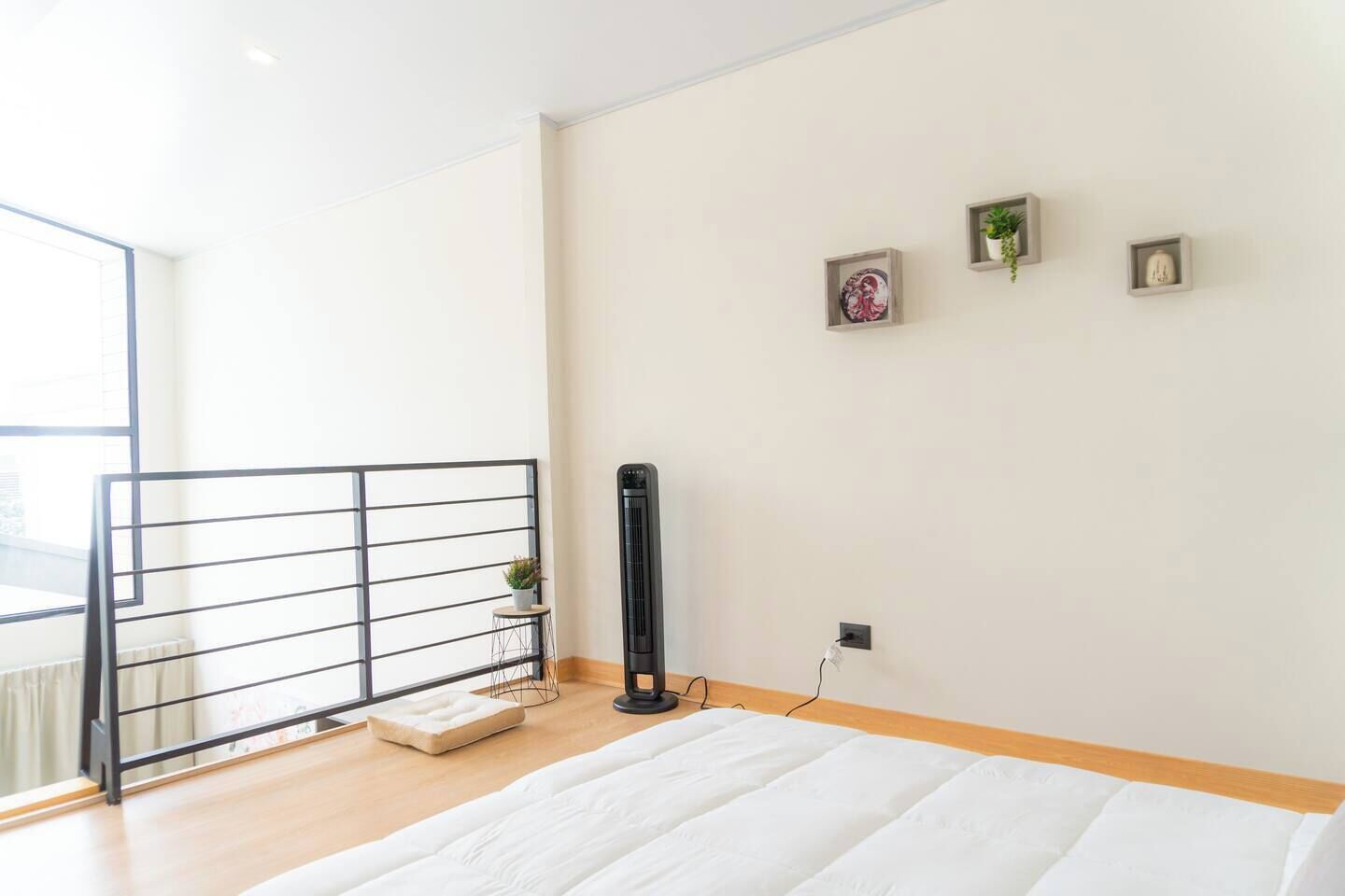 Une chambre moderne avec une grande fenêtre, un radiateur noir, un matelas blanc et une petite plante posée sur une table de chevet.