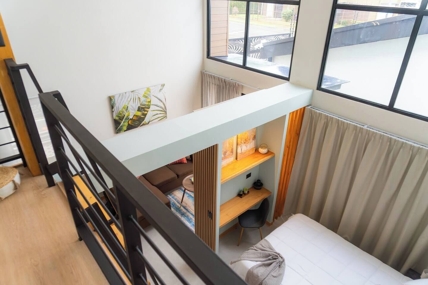 A loft-style bedroom with a loft bed, a desk, and a window overlooking a courtyard.