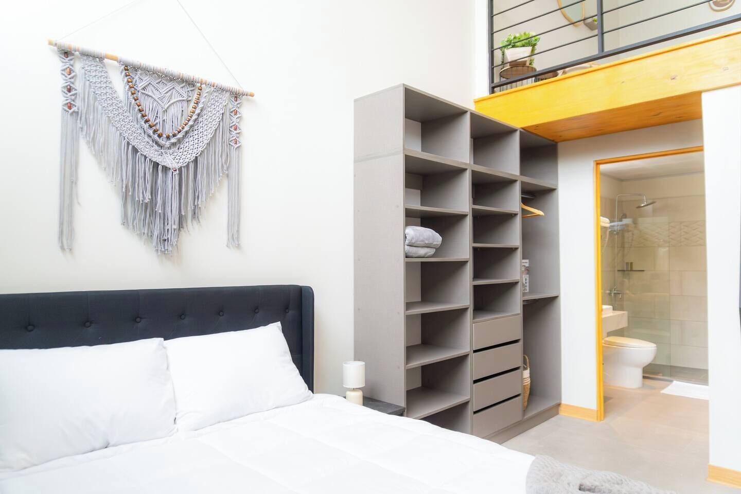 A modern bedroom with a bed, a grey wardrobe, and a macrame wall hanging.
