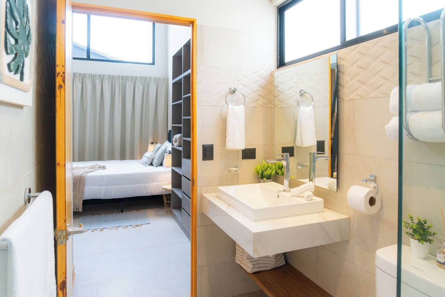Un baño moderno con un espejo grande, lavamanos blanco y zona de ducha.