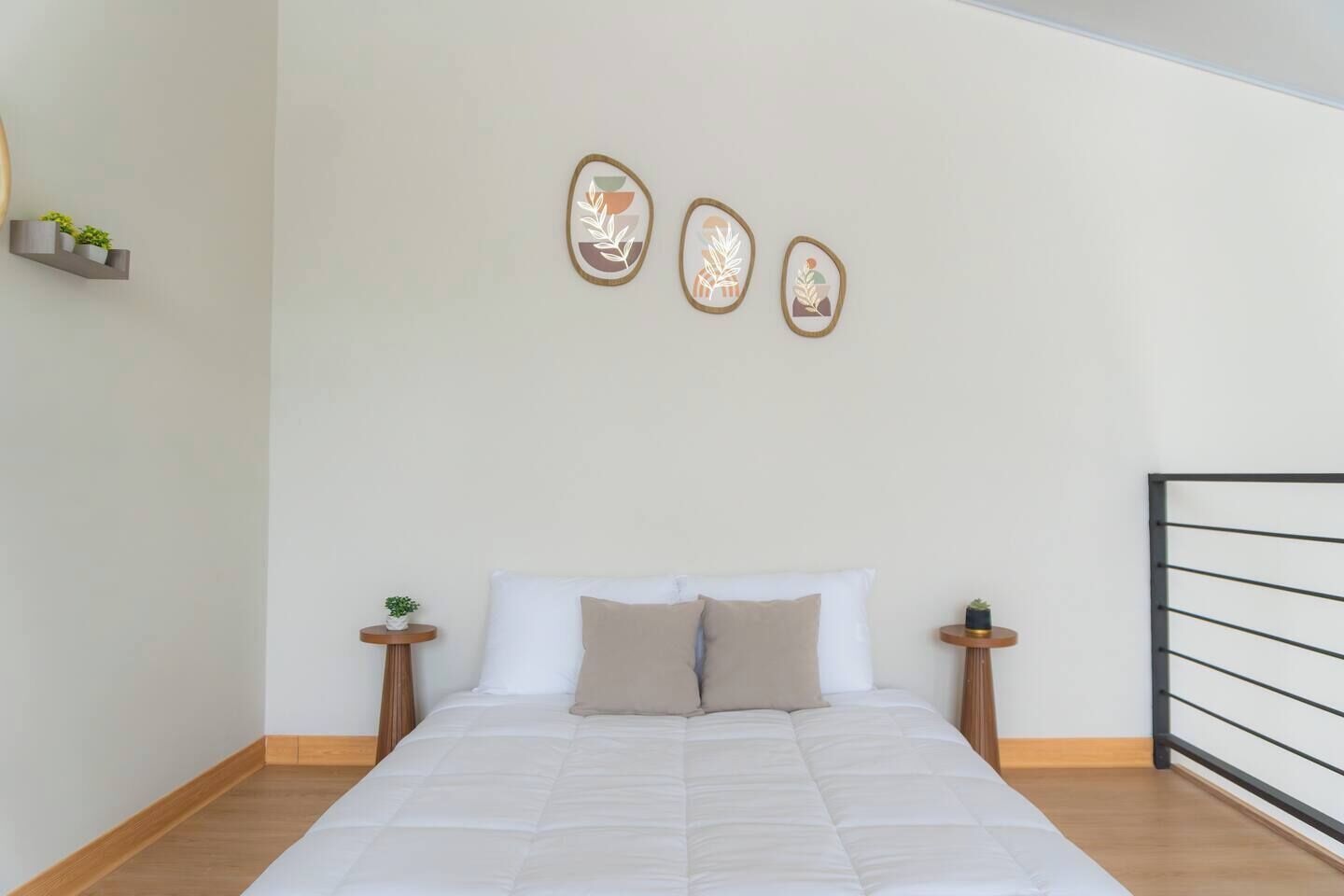 Une chambre à coucher comprenant un lit, deux tables de chevet, une étagère murale avec des plantes et trois œuvres d’art accrochées au mur.