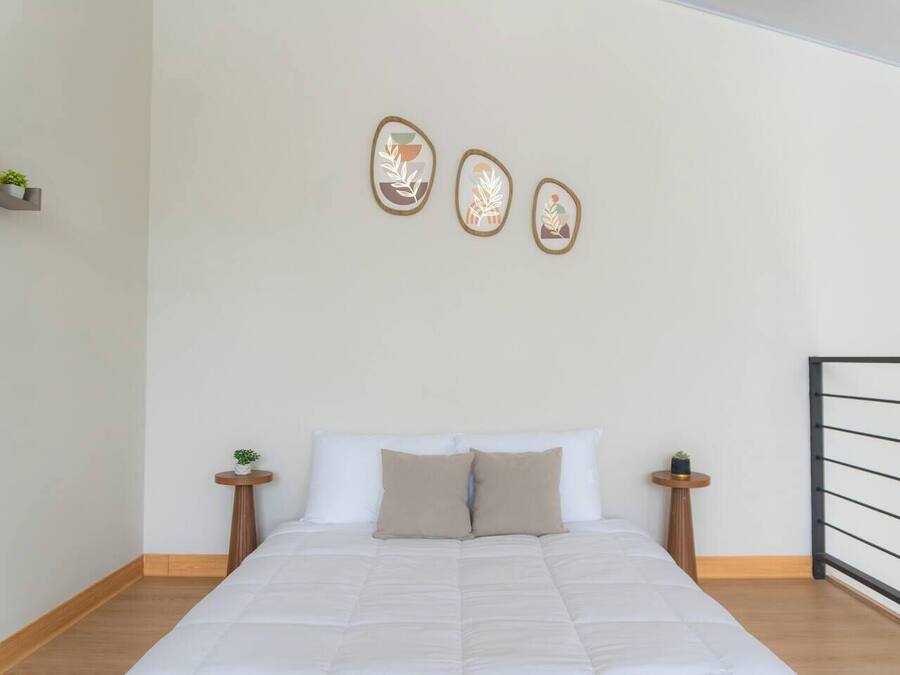Un dormitorio con cama, dos mesitas de noche, un estante en la pared con plantas y tres obras de arte.