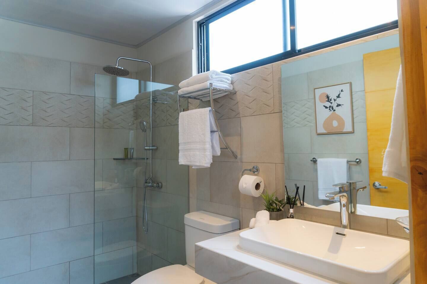 A modern bathroom with a glass-enclosed shower, a toilet, and a sink with a large mirror.