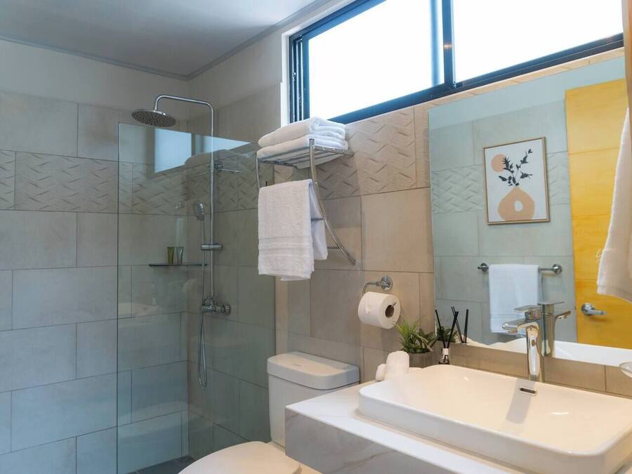 A modern bathroom with a glass-enclosed shower, a toilet, and a sink with a large mirror.