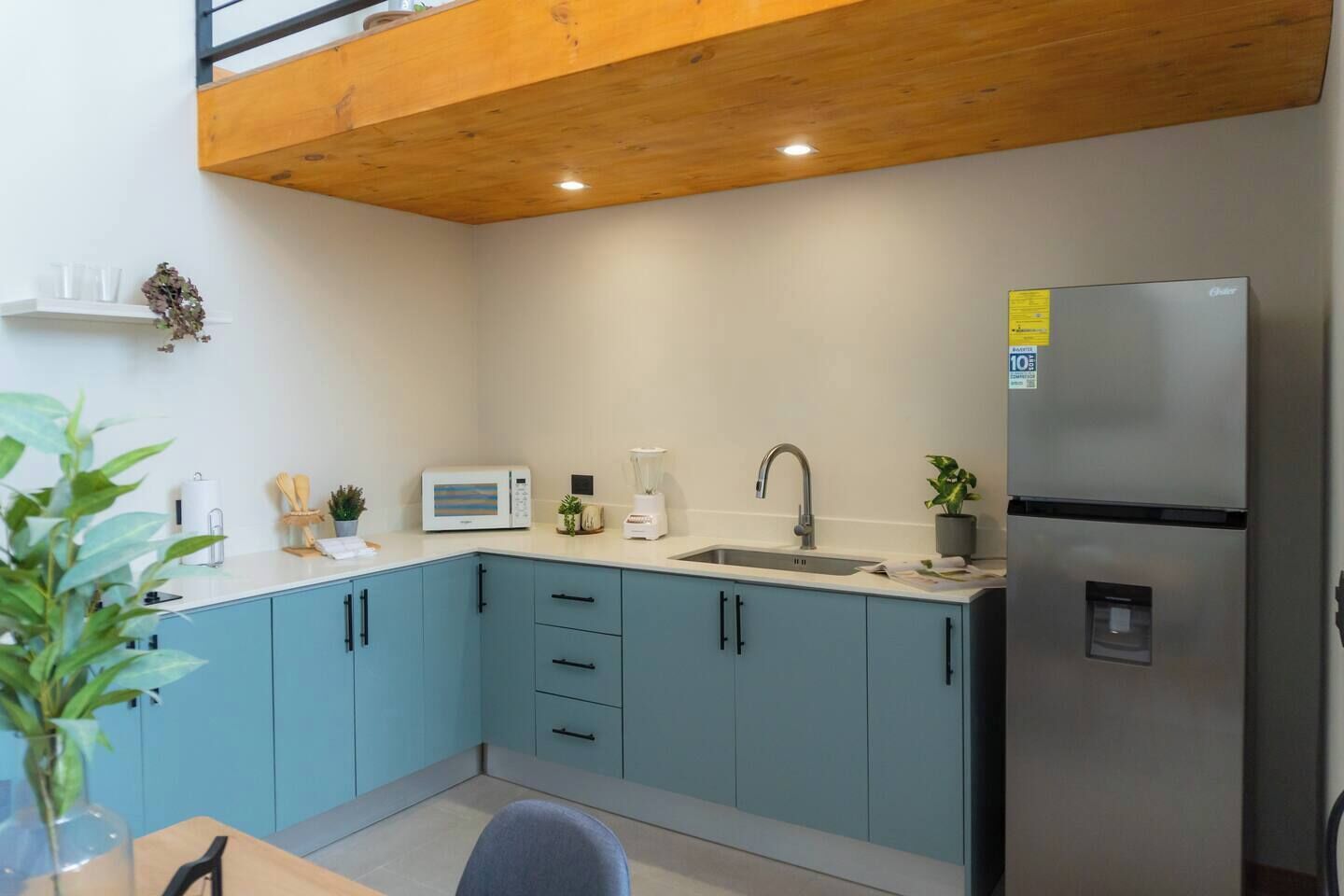 Een moderne keuken met lichtblauwe kastjes, een roestvrijstalen koelkast, een magnetron en een spoelbak.