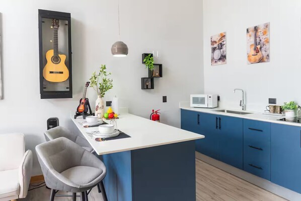 Eine moderne Küche mit Kochinsel, blauen Schränken, einer weißen Arbeitsplatte und einer an der Decke hängenden Gitarre.