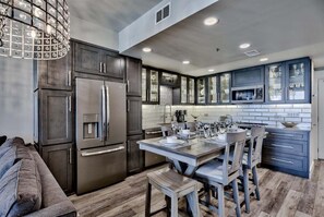 A modern kitchen with dark cabinetry, stainless steel appliances, and a dining area with a wooden table and chairs. - Leeward Key # 504 | Gulf Views + Pool & Elevator! (Miramar Beach)