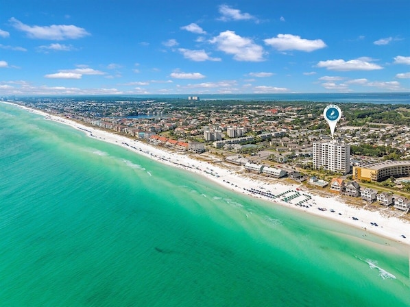 An aerial view of a coastal city with a beach, buildings, and a clear sky.