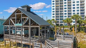 Un hôtel situé en bord de mer, doté d’une structure de terrasse en bois et d’une enseigne indiquant « Emerald Shores ».