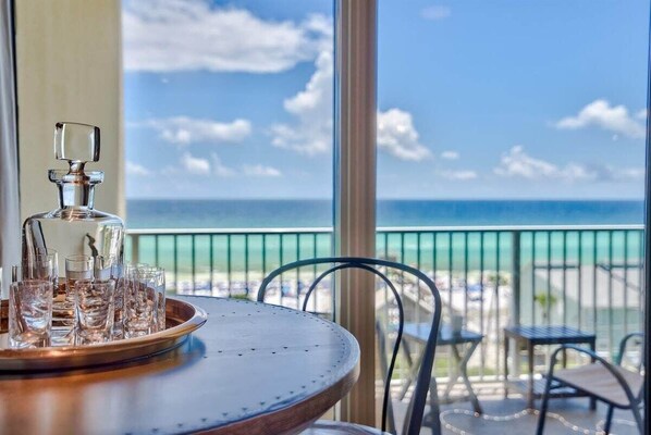 A table with a tray of glasses and a bottle, overlooking a beach with a clear sky.