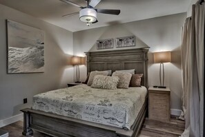 A bedroom with a bed, two bedside tables, a ceiling fan, and a large painting on the wall.
