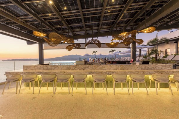 Espaço bar com vista para o mar, mesas ao ar livre e design moderno.