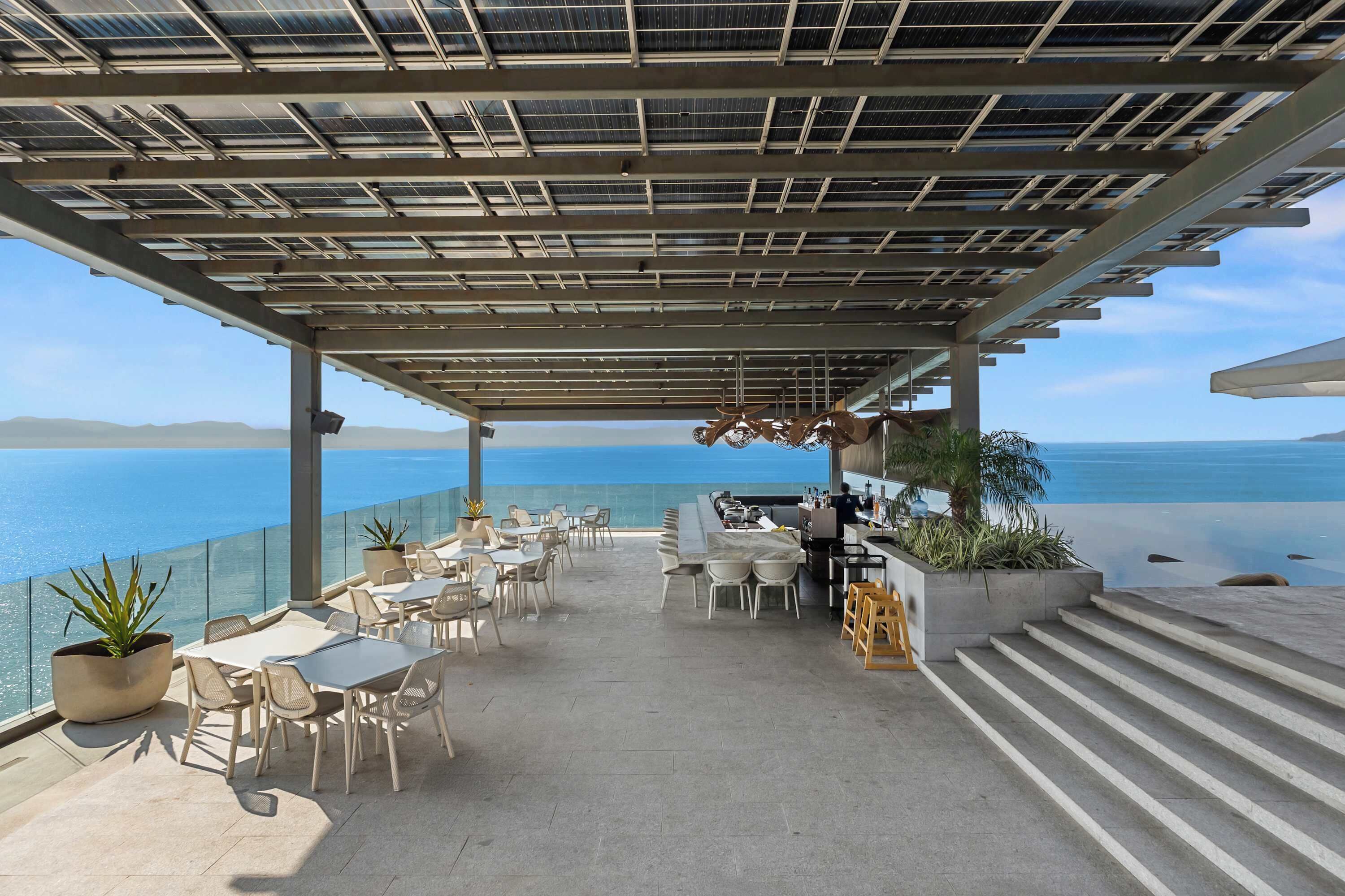 Une terrasse sur le toit, aménagée avec des tables et des chaises, un espace bar et une vue sur la mer.