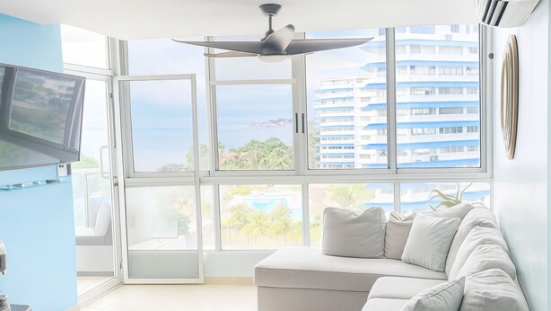 Una sala de estar moderna con un ventanal grande, un ventilador de techo y un televisor de pantalla plana.