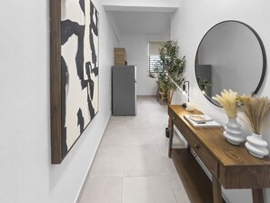 A hallway with a wooden desk, a mirror, and a refrigerator.