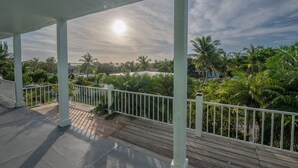 Ein überdachter Außenbereich mit Holzdeck, weißen Geländern und Blick auf Palmen und Grünflächen.