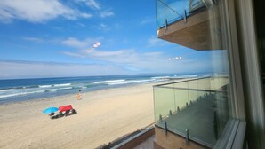 Vista a la playa desde un balcón, cielo despejado, arena y algunas sombrillas.