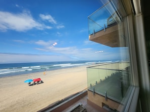 A beach view from a balcony with a clear sky, a sandy beach, and a few umbrellas.