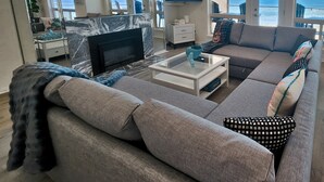 Una sala de estar moderna con un sofá, una mesa de centro y un televisor. Amplias ventanas ofrecen vistas al océano.