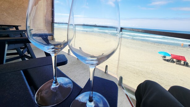 Dos copas de vino vacías sobre una mesa con vista a la playa y el océano.